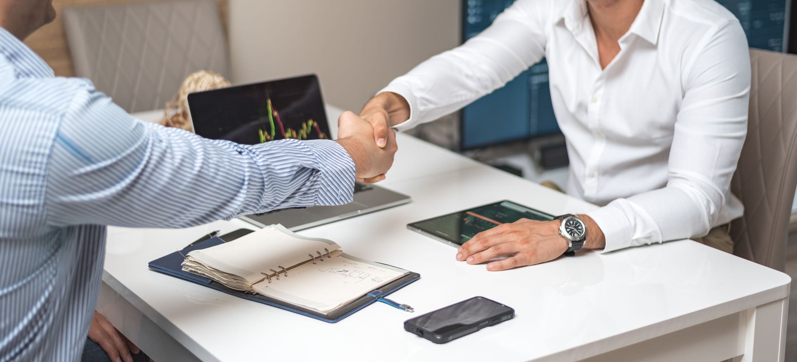 Two businessmen shaking hands in a modern office, indicating a successful deal or agreement.