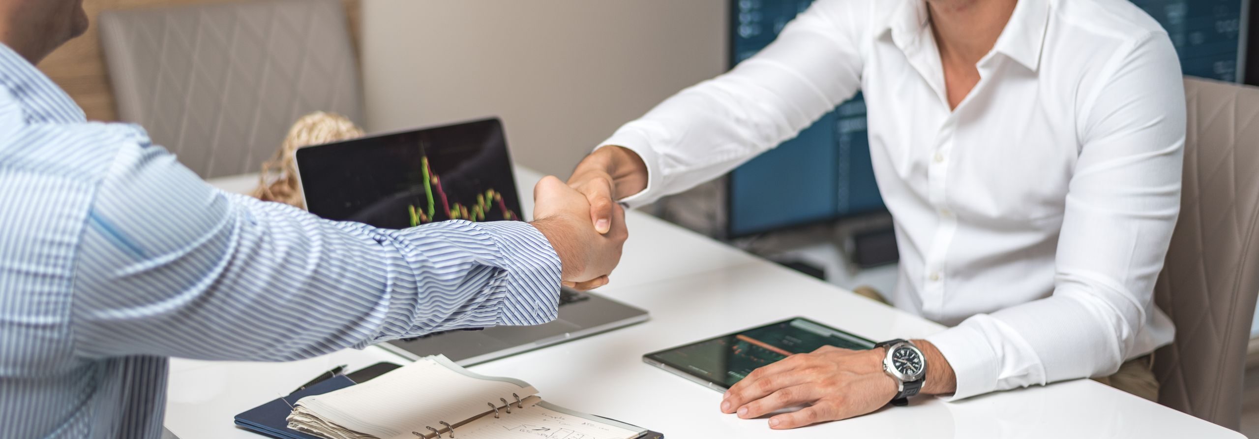 Two businessmen shaking hands in a modern office, indicating a successful deal or agreement.