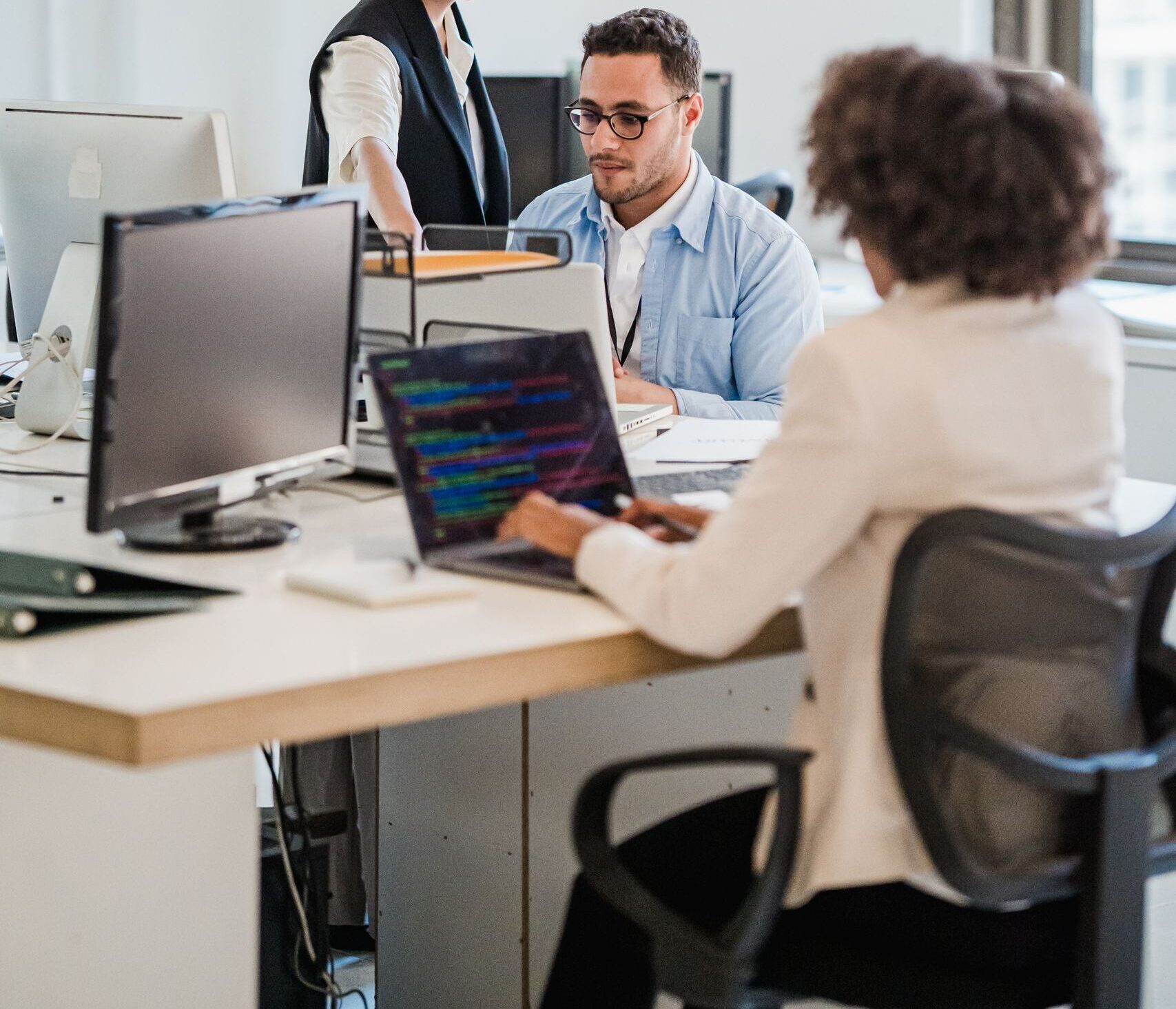 Business team working collaboratively in a modern office setting with computers and laptops.