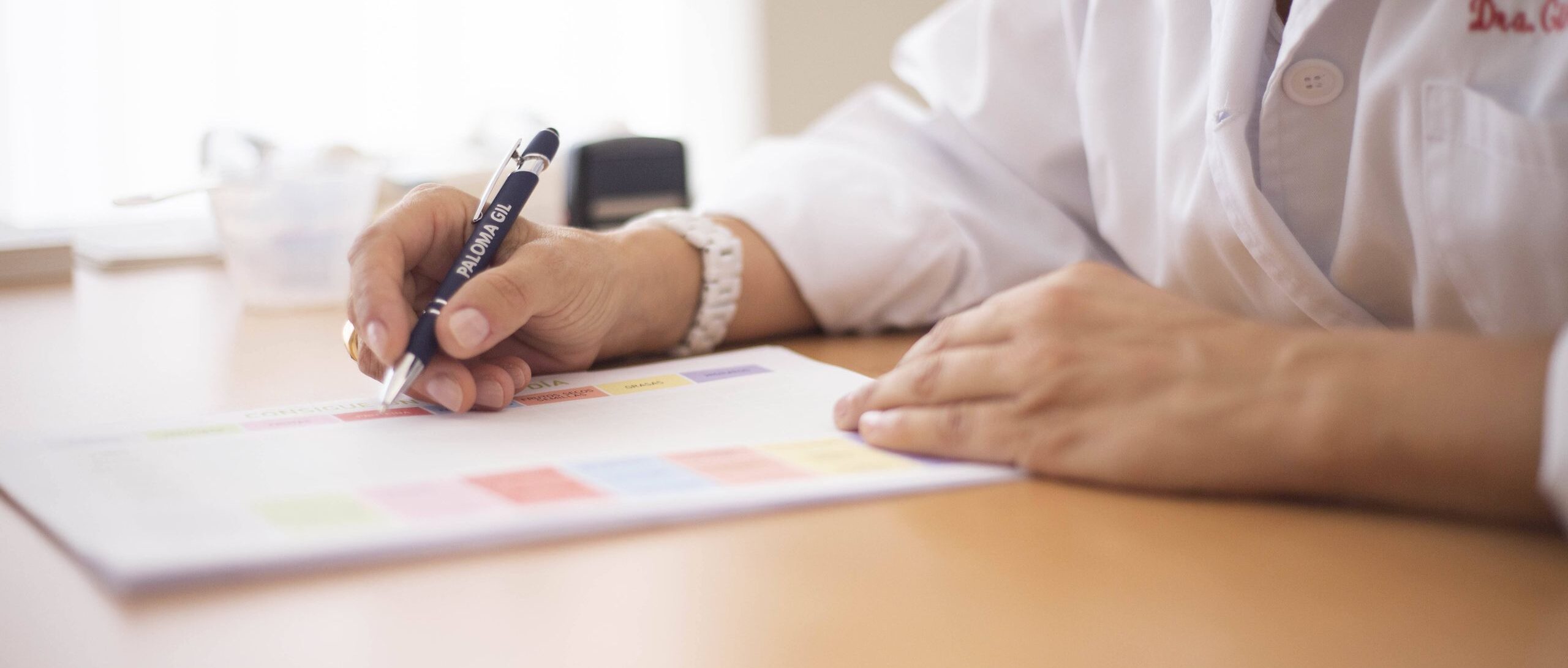 Close-up of a female doctor writing a prescription at a desk in an office setting.