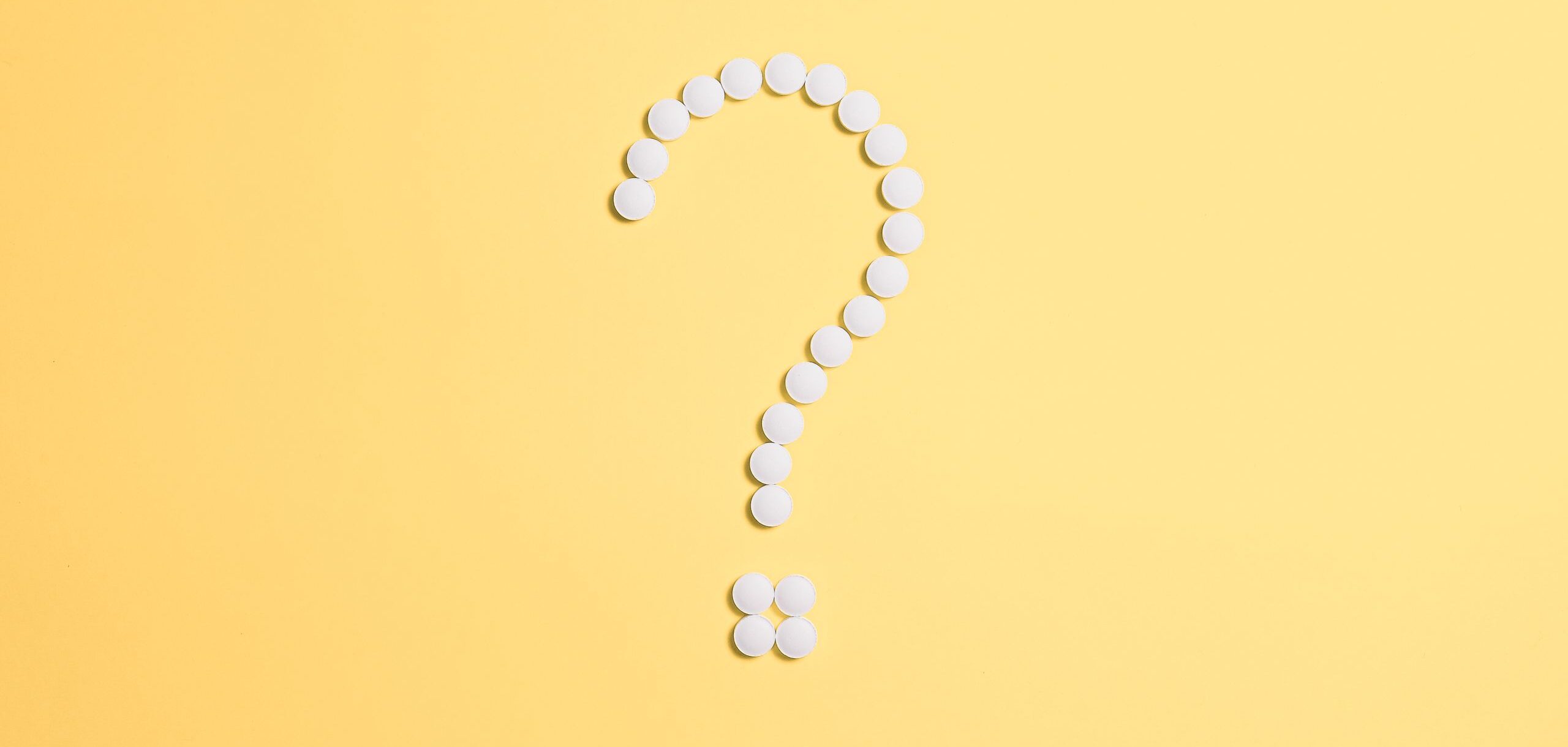 White pills arranged into a question mark shape on a vibrant yellow background.